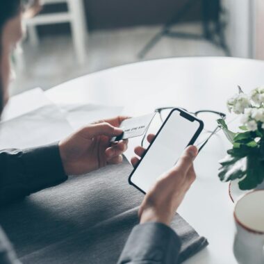 A man holding a credit card and smartphone at a table, engaging in online payment indoors.